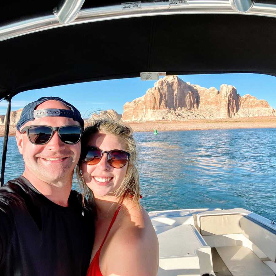 Couple take a selfie together while on a boat with mountains behind them