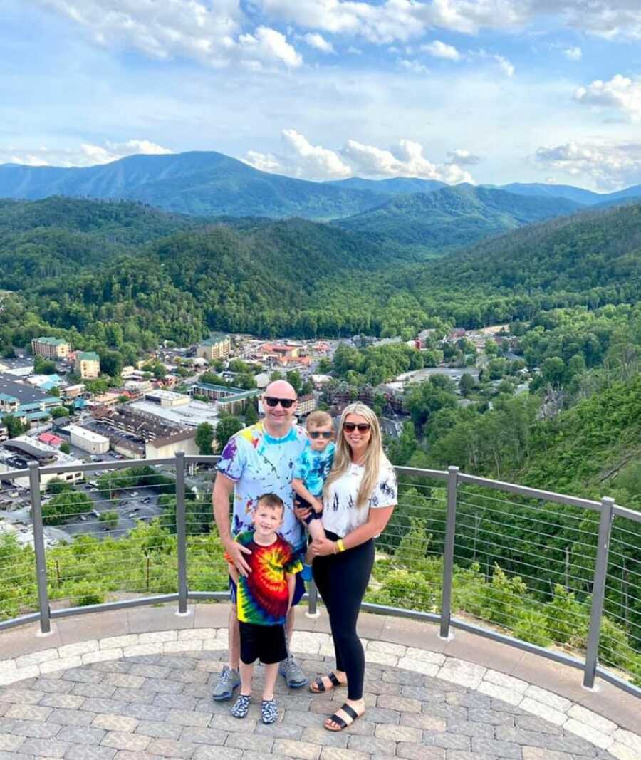 Blended family take a group photo with a gorgeous view of a town below them