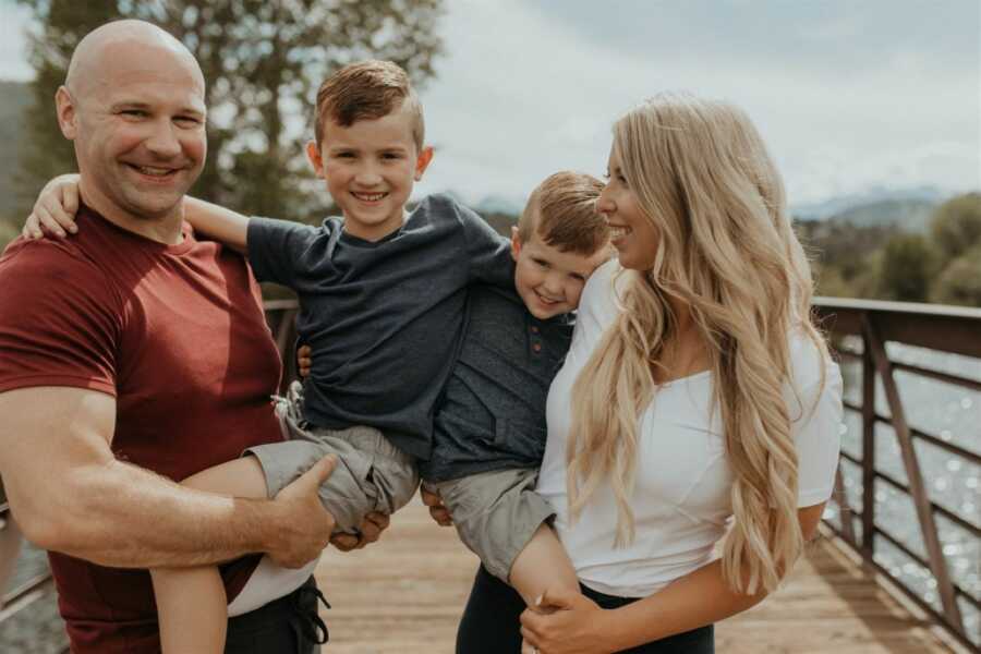 Parents hold their two sons in matching outfits while taking family photos on a bridge