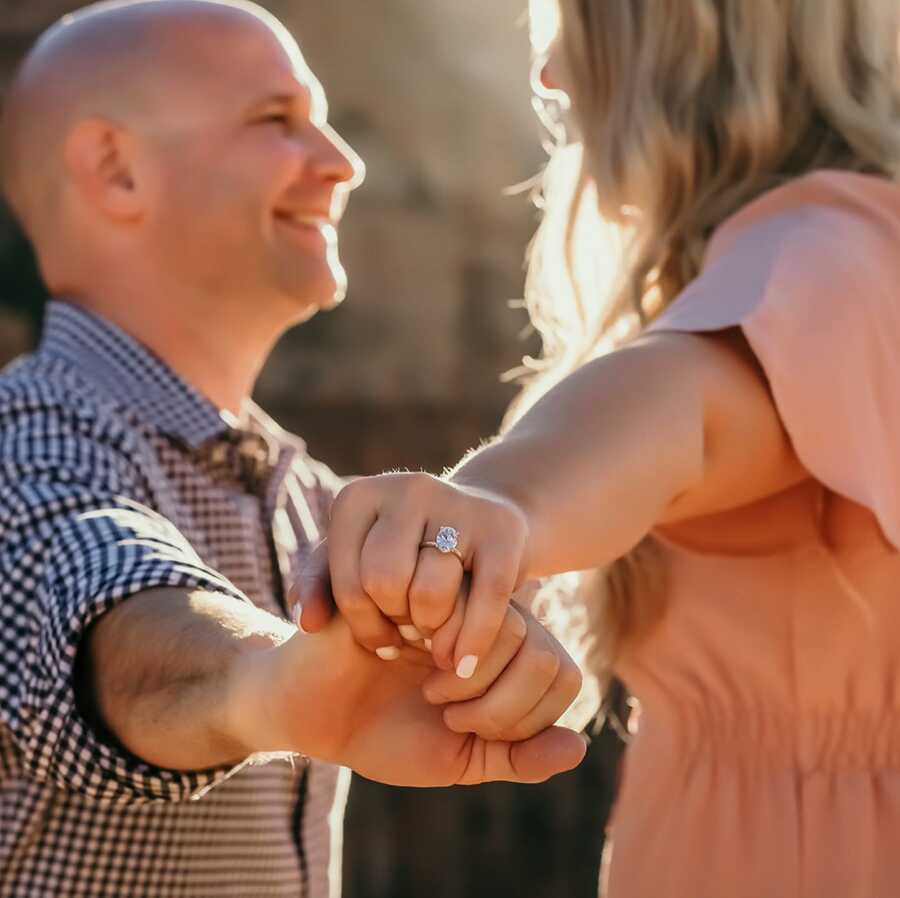 Newly engaged couple smile and hold hands while showing off the engagement ring