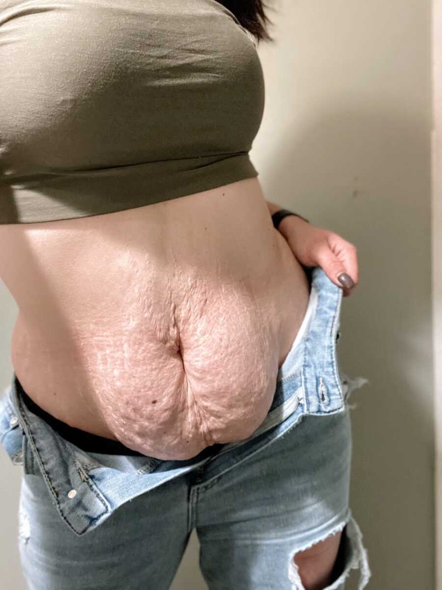 Mom holds up jeans while taking a photo of her stomach