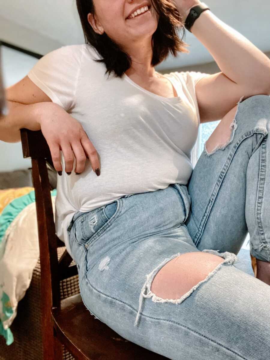 Mom takes a photo of her sitting naturally in a chair in white shirt and jeans