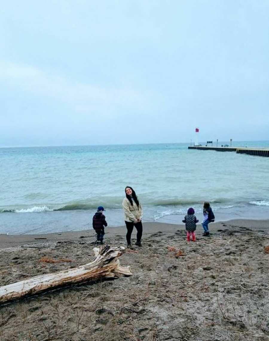 Mom smiles for a photo while her kids run around and play on the beach