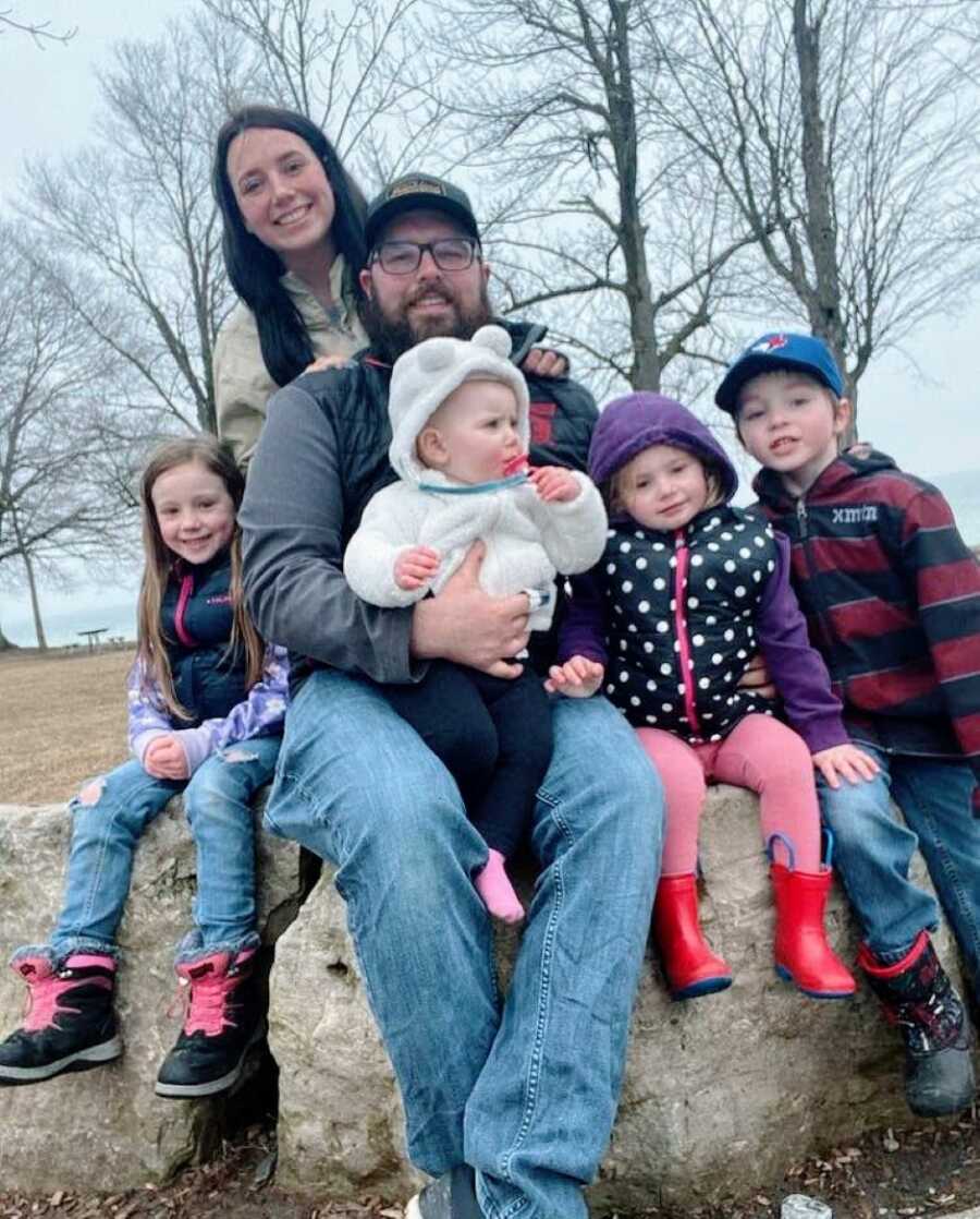 Family of six take a group photo together while sitting on rocks during a family outing