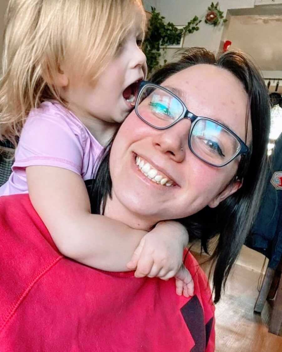 Mom and daughter take a silly selfie together while her daughter climbs on her back