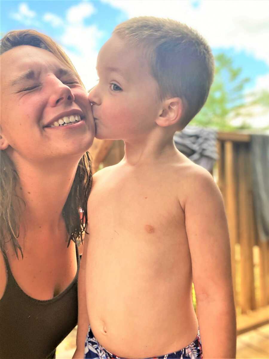 Mom receiving a kiss on the cheek from her shirtless toddle son 