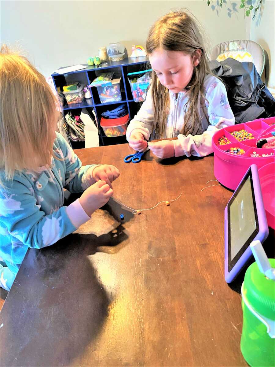 toddlers sitting at the table making beads jewelry and watching cartoons on an iPad