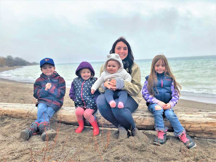 Outdoor family portrait of a mom and her 4 kids sitting on a branch in front of a lake