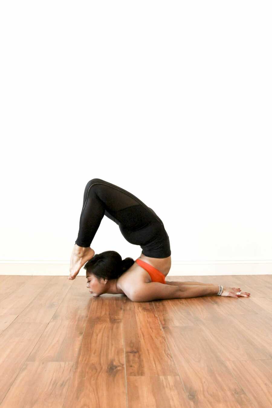 Yoga instructor does a yoga pose during a photoshoot in red sports bra and black leggings