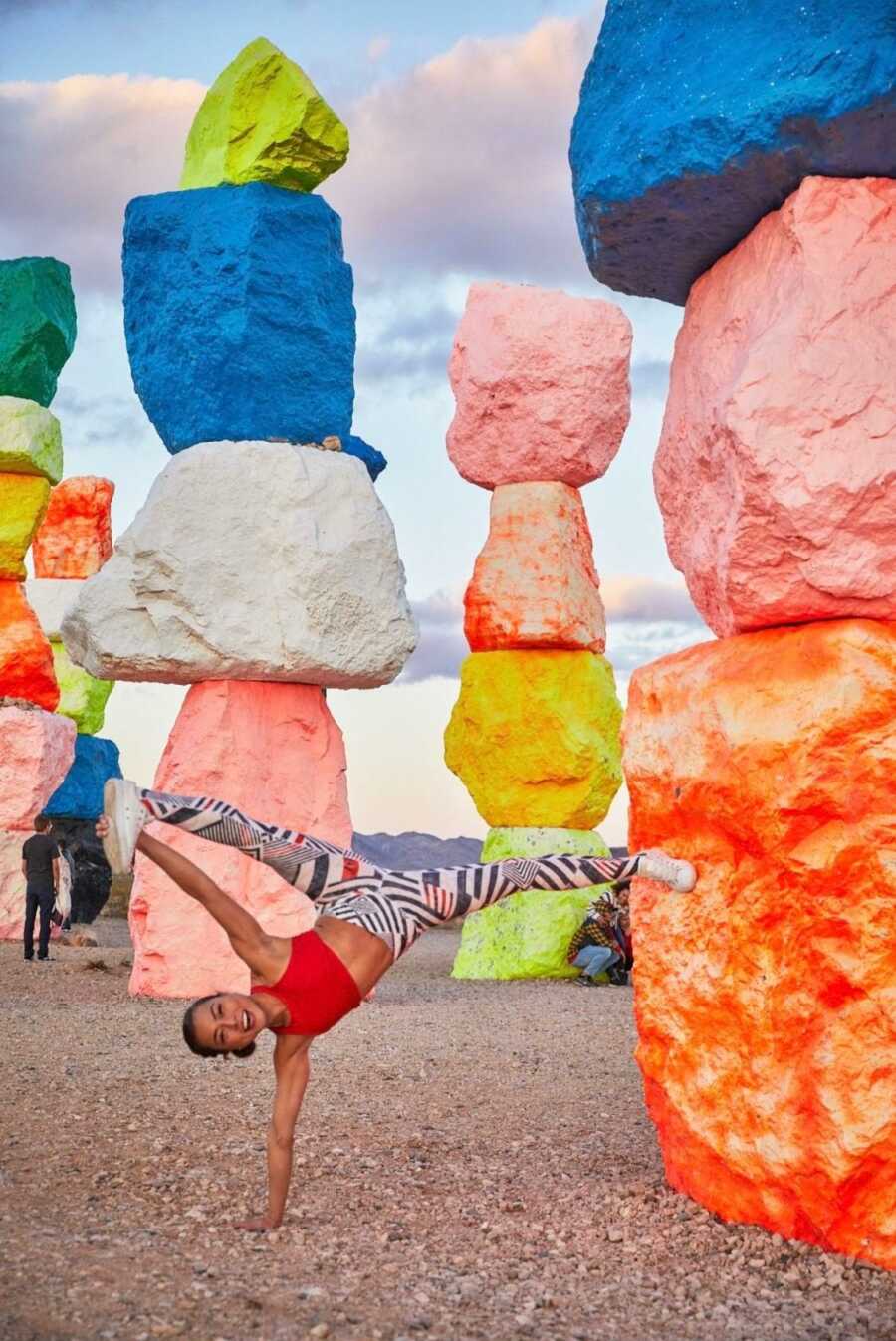 Woman strikes yoga pose while leaning on colorful rocks with more colorful rocks behind her