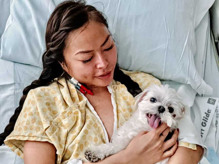Woman paralyzed from Transverse Myelitis holds her white dog while in the hospital