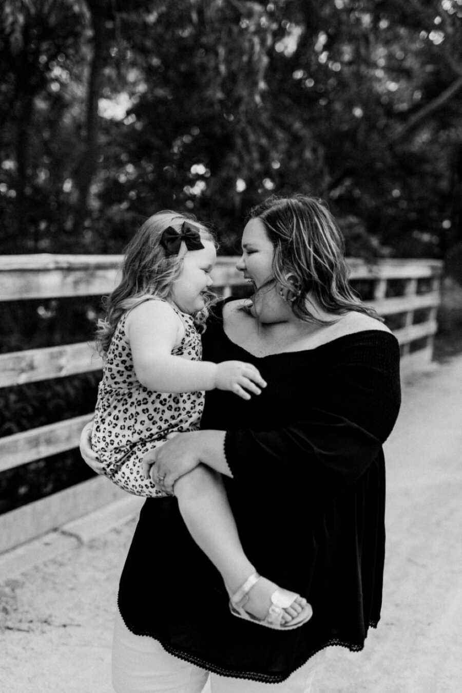 Mom and daughter take candid photo dancing on a bridge during family photoshoot