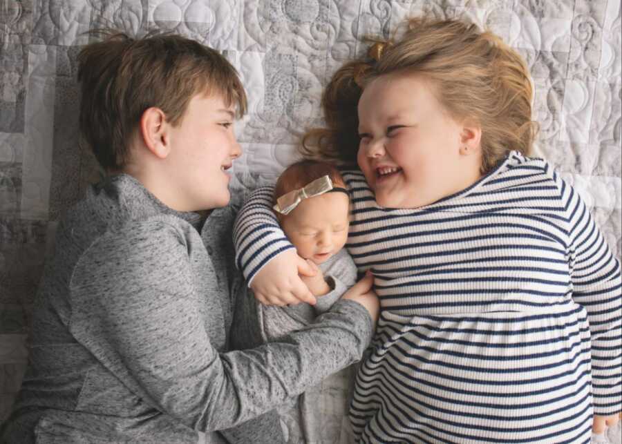 Three siblings smile and laugh together while wearing matching gray outfits