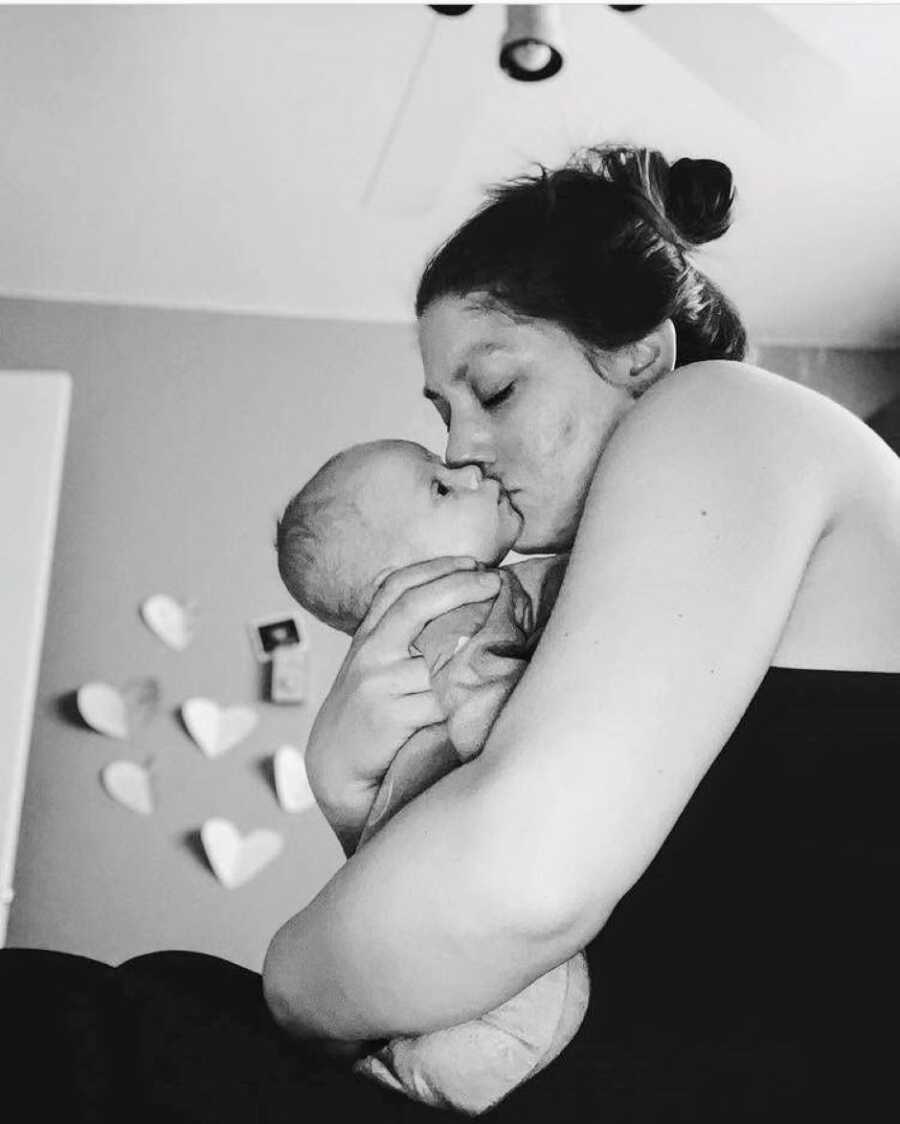 Mom kisses newborn child on the cheek while they enjoy time alone bonding