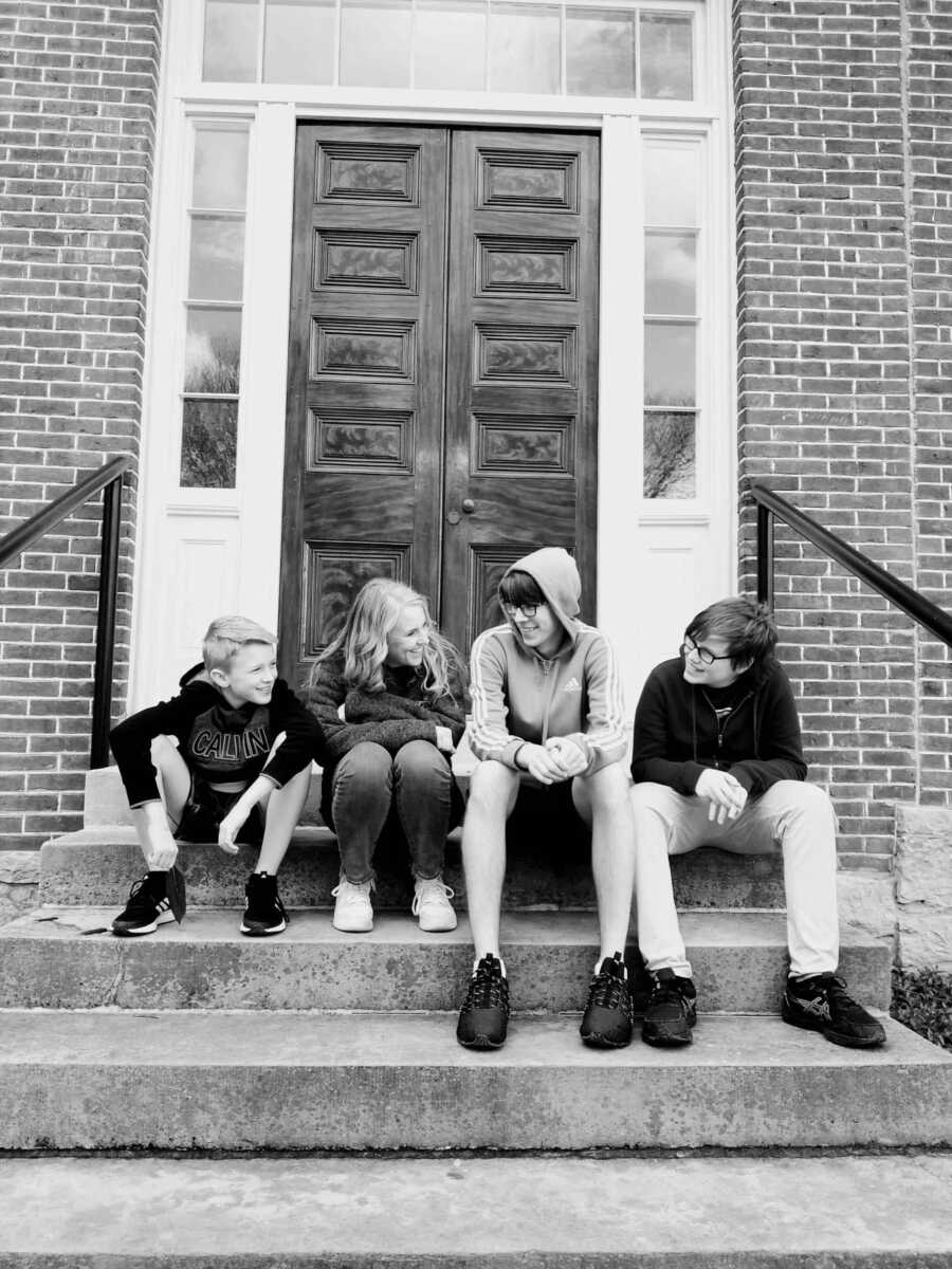 Mom sits on steps with her three sons as they laugh together