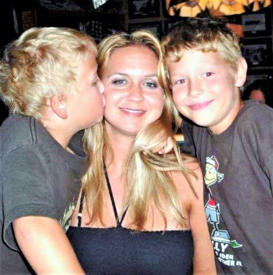 Mom sitting in-between her two young sons while one gives her a kiss on the cheek