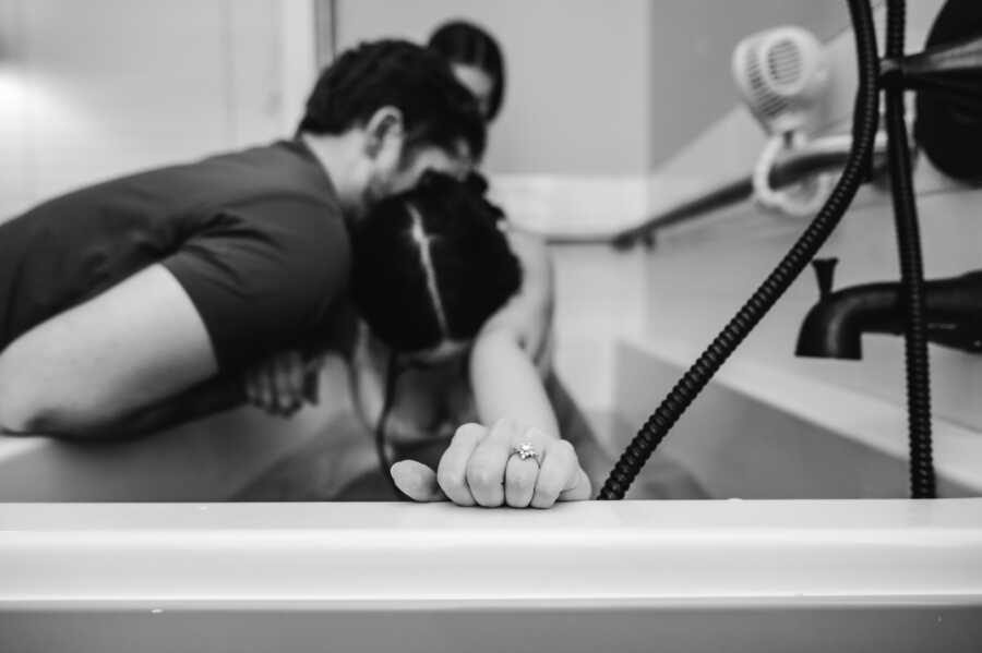 Pregnant woman having strong contractions in a bathtub while her husband comforts her 