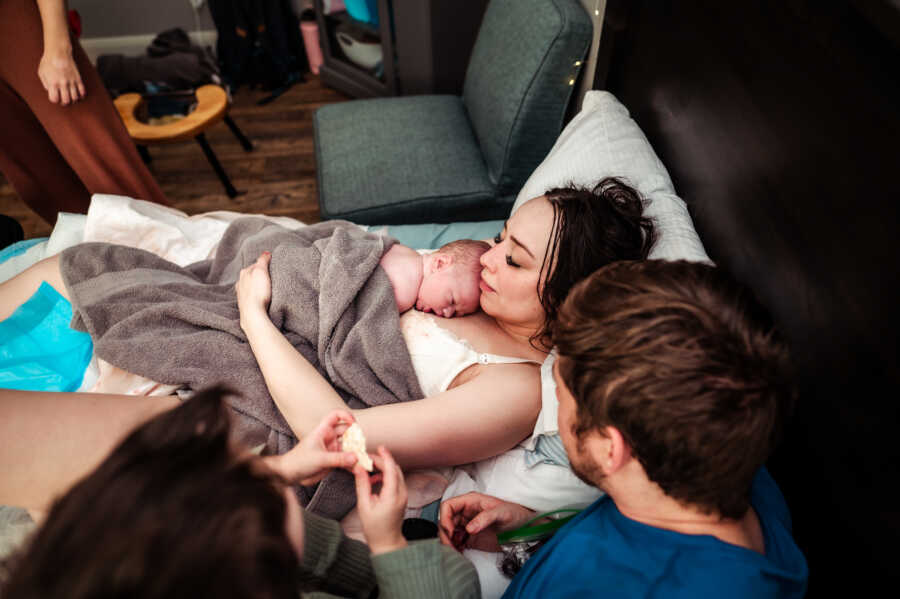 Mom resting with her newborn baby on her chest and her husband and son next to her right after delivery 