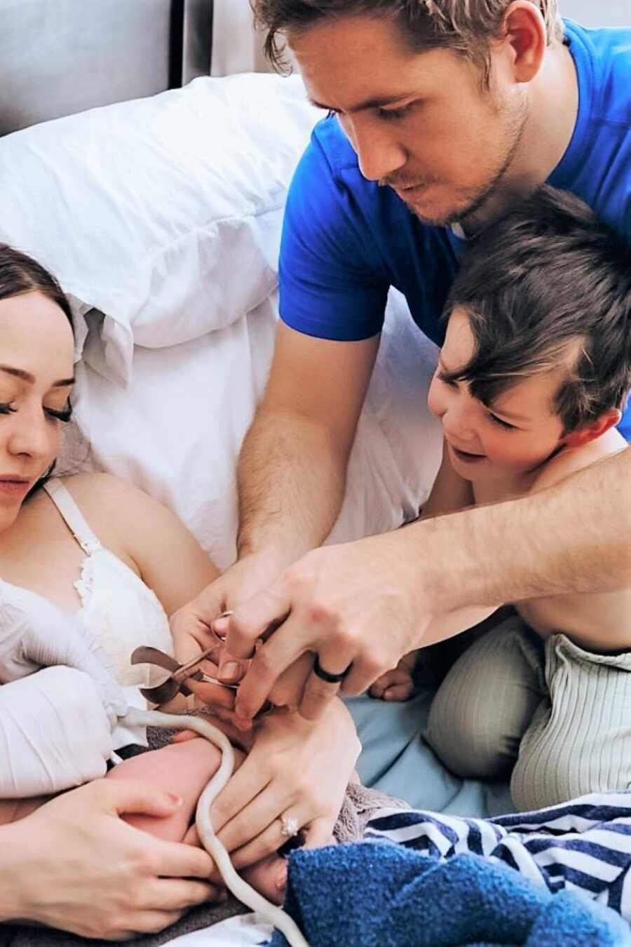 Mom holding newborn baby while dad and brother cut the umbilical cord 