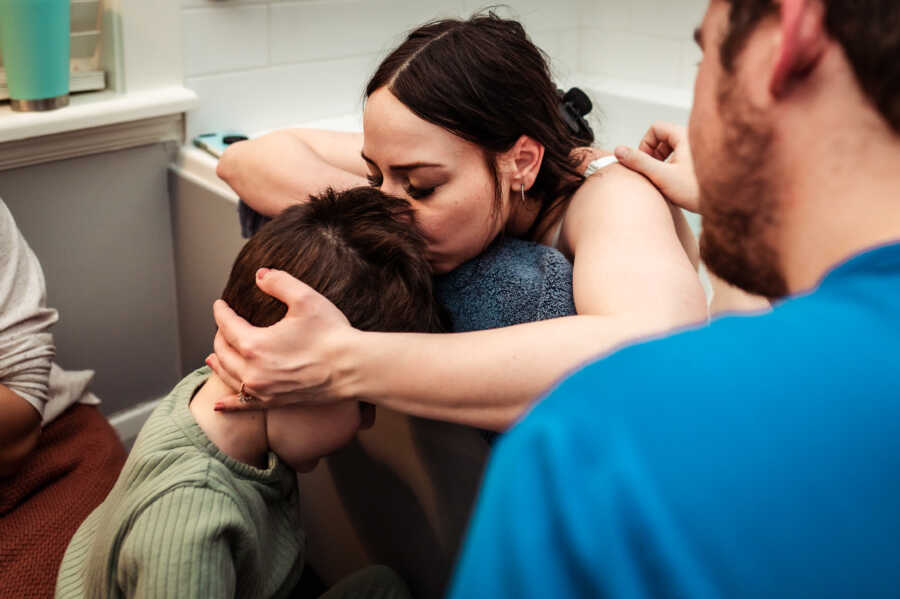 Mom kissing son's forehead while her husband comforts her in the bathtub during contractions