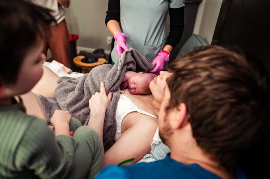 Mom resting with her newborn baby on her chest and her husband and son next to her right after delivery 