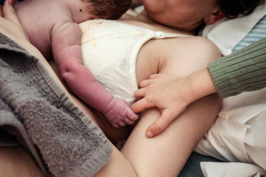 Mom holding her newborn son in her chest while baby brother holds his hand 