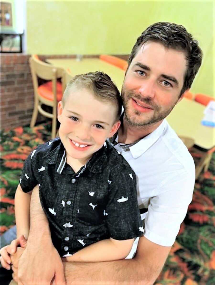 Son sitting on his dad's lap and both smiling 