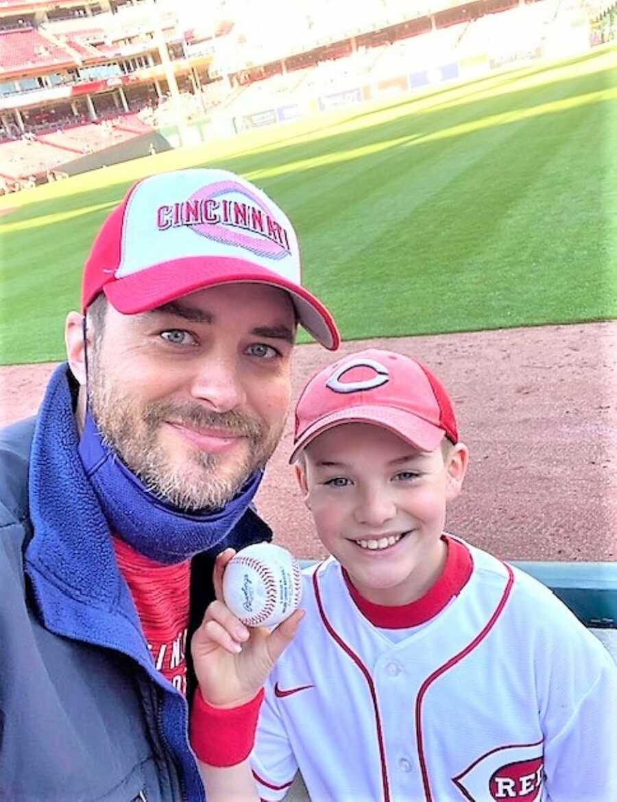 father and son at a baseball game with son holding a baseball ball 