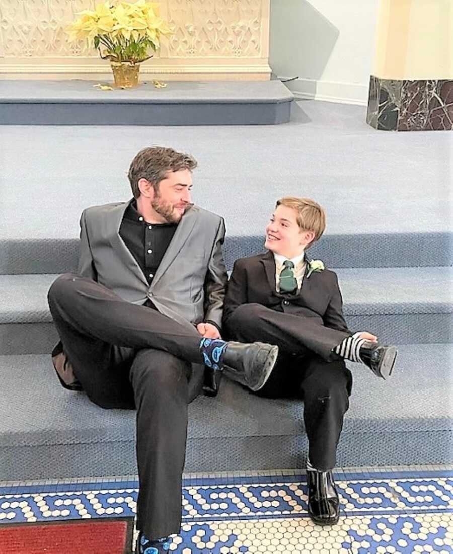 father and son wearing suits and sitting with their legs crossed looking at each other