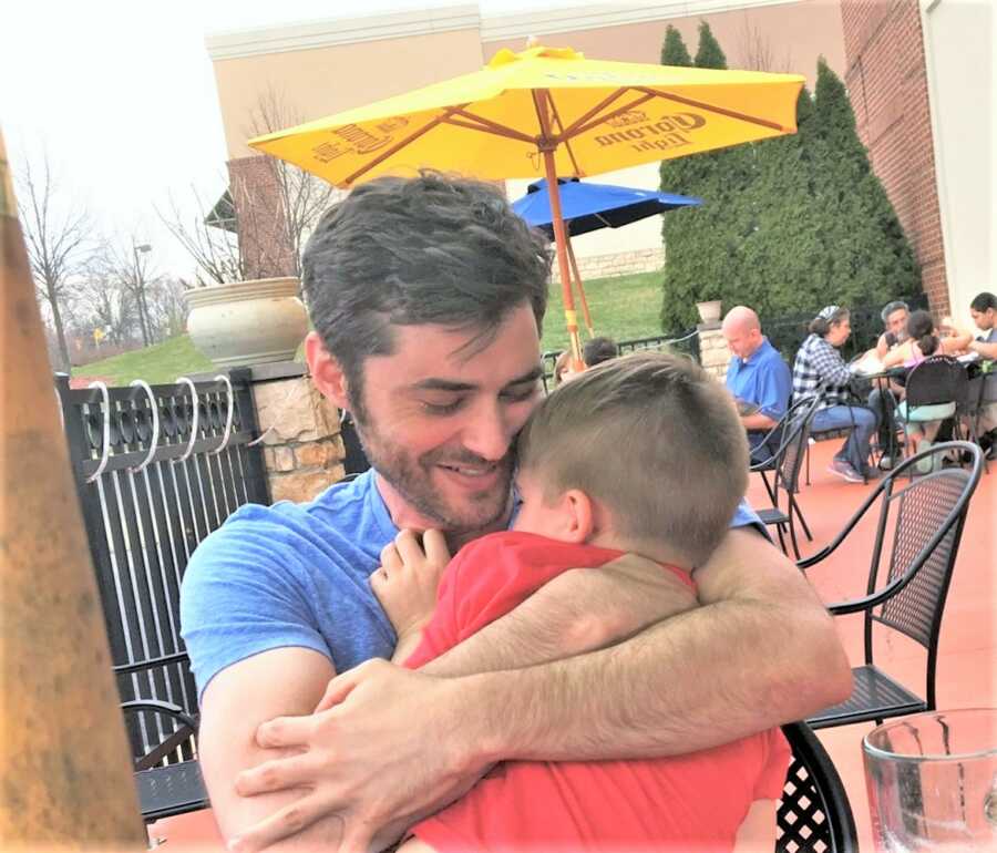 Man cuddles with his adoptive son while they sit outside at a restaurant for lunch