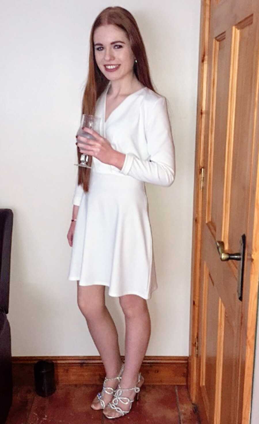 Young college student poses for a photo in a white dress while holding a glass of champagne