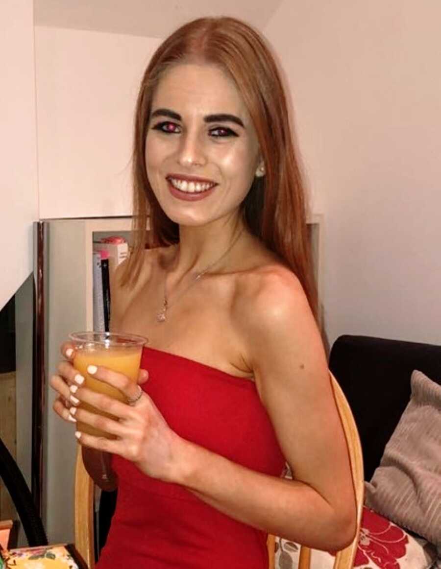 Young college student recovering from an eating disorder smiles for a photo in a red dress while out at a party