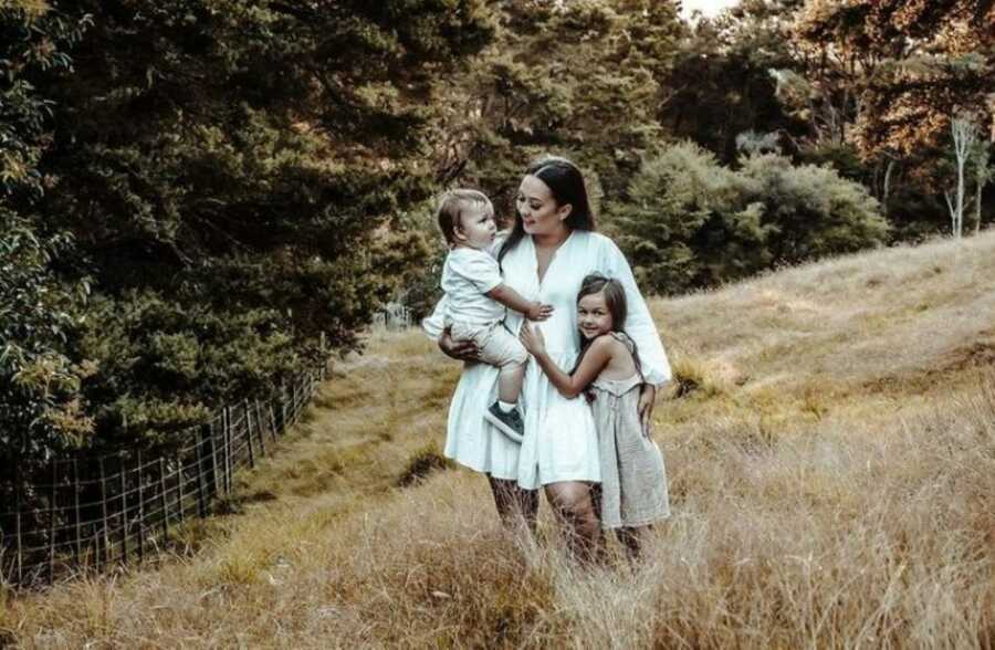 Mom of two stands with her children in a field during a family photoshoot
