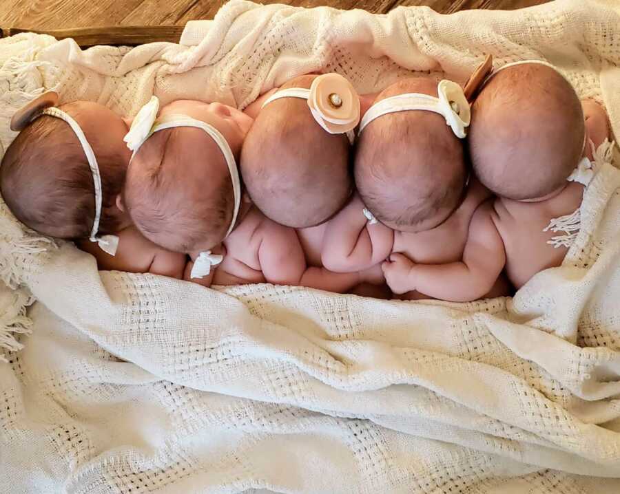 Quintuplet sisters cuddle under a blanket together in matching headbands