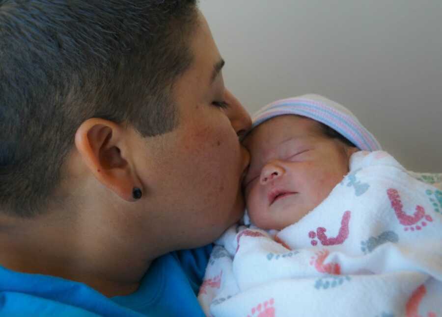 Mom kisses her newborn daughter on the forehead while she sleeps in her arms