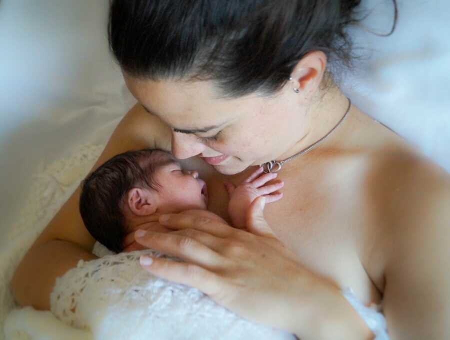 Mom looks down at her newborn daughter sleeping on her chest during skin-to-skin contact time