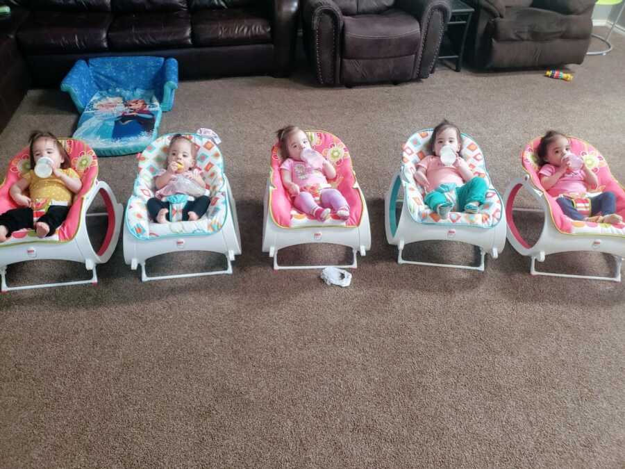Quintuplets all drink from bottles while sitting in rockers in the living room