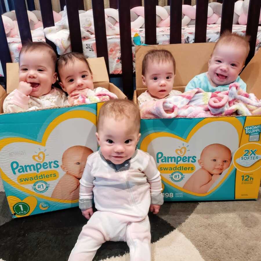 Quintuplets smile while sitting in Pampers Swaddlers diaper boxes