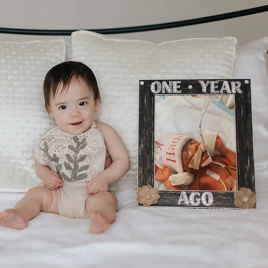 Hadin sits next a photo of herself as a newborn, showing how much she's grown in a year