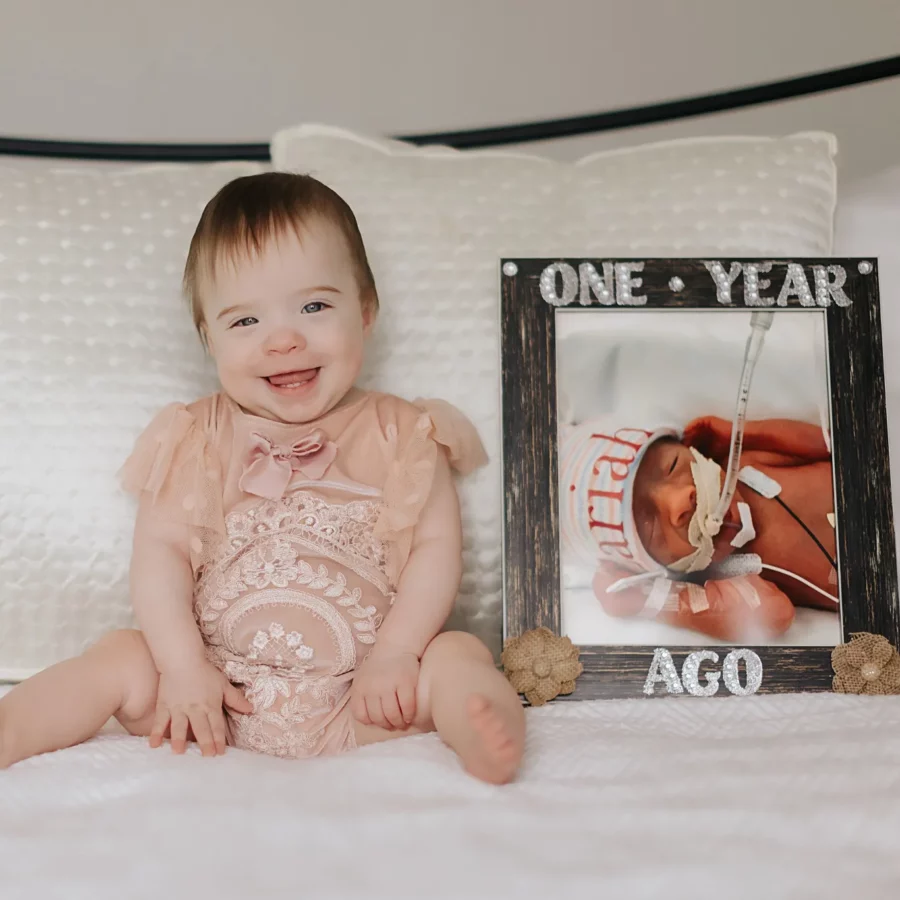 Zariah sits next a photo of herself as a newborn, showing how much she's grown in a year