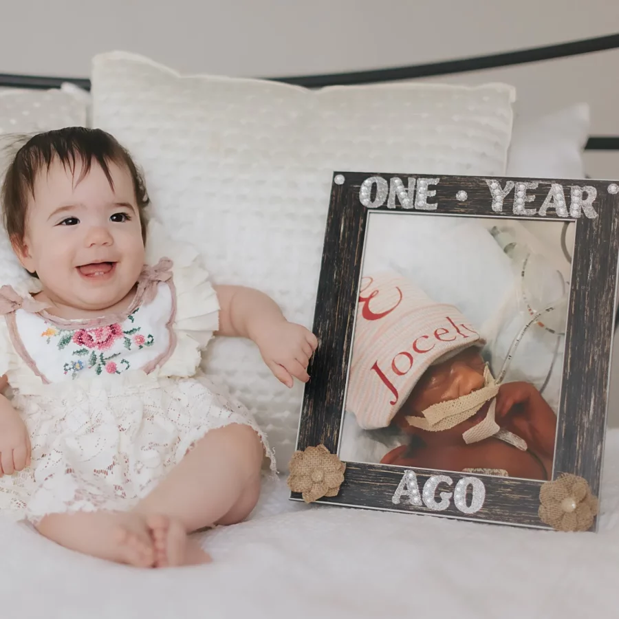 Jocely sits next a photo of herself as a newborn, showing how much she's grown in a year