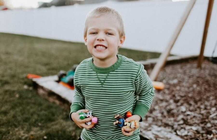 Little boy with autism smiles for a photo while playing in his backyard with Paw Patrol toys