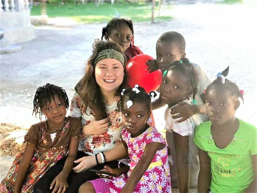 white girl in her twenties sitting with six African American kids who are hugging her 