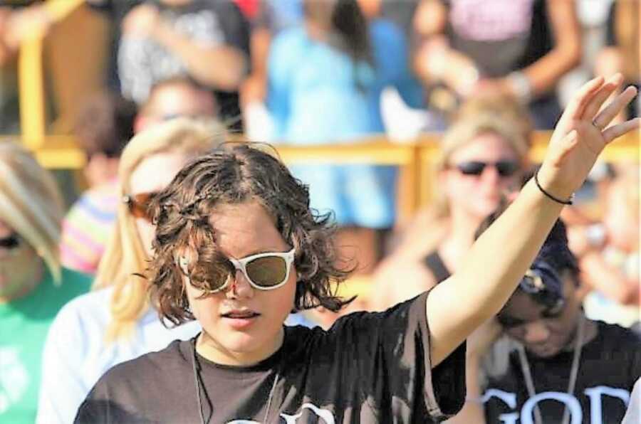 teenage girl holding her hand up praying to God at a religious event 