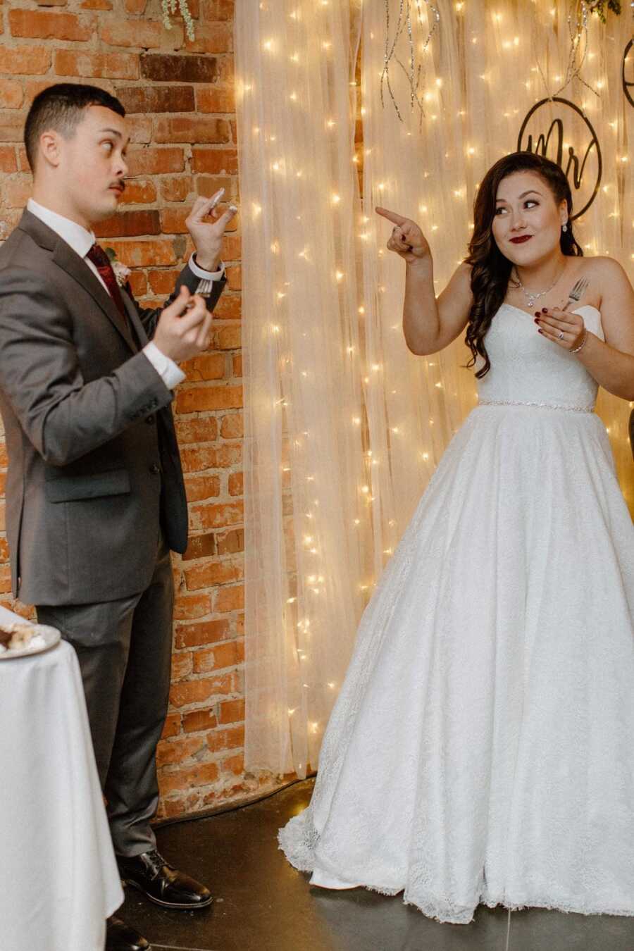 bride and groom humorously signaling each other during their wedding reception 