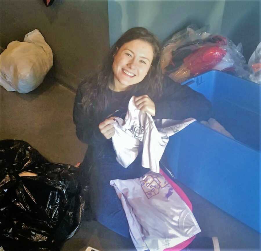 woman in her twenties sitting on the floor smiling and organizing a bin with clothes