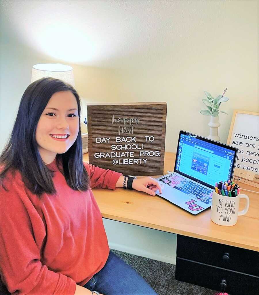 young woman sitting on a desk with a laptop and a sign that says "HAPPY FIRST DAY BACK TO SCHOOL!"