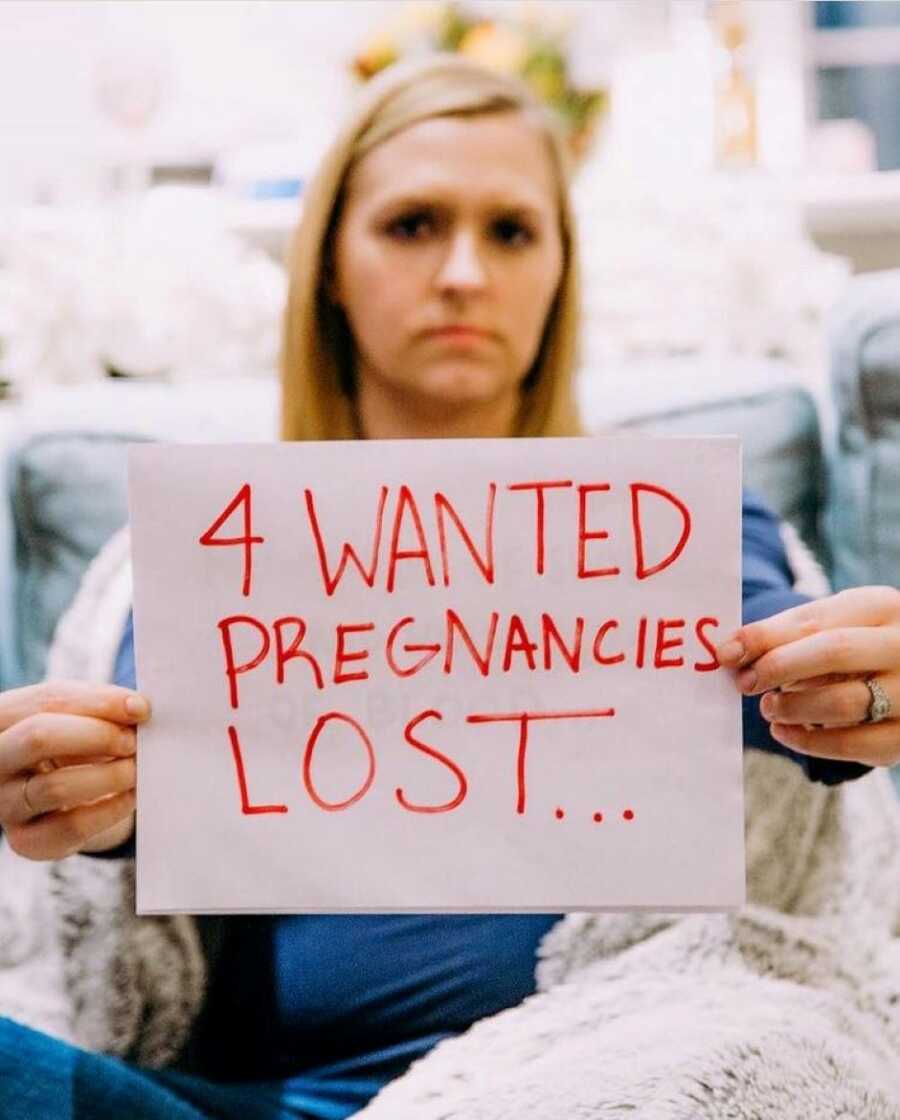 Woman looking solemn holds up sign that reads "4 wanted pregnancies lost"