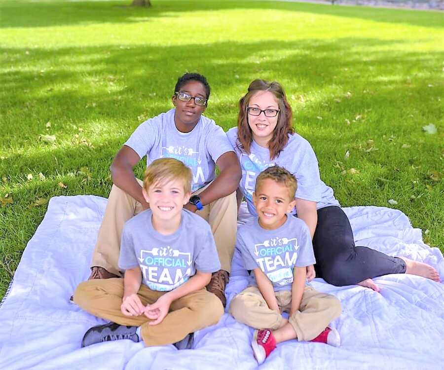 Blended LGBT family take photos together on a blanket in a park in matching t-shirts