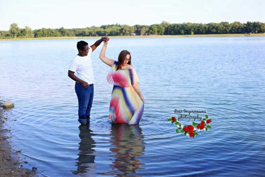 Lesbian couple take photo together in a lake while one spins the other around in the water